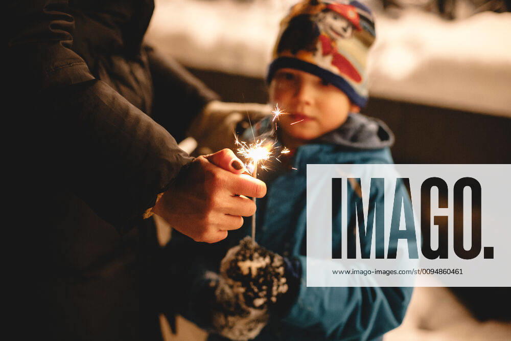 Mother igniting sparkler held by her son outdoors in winter Kyiv, Ukraine CR_DMBE191028-208601-01
