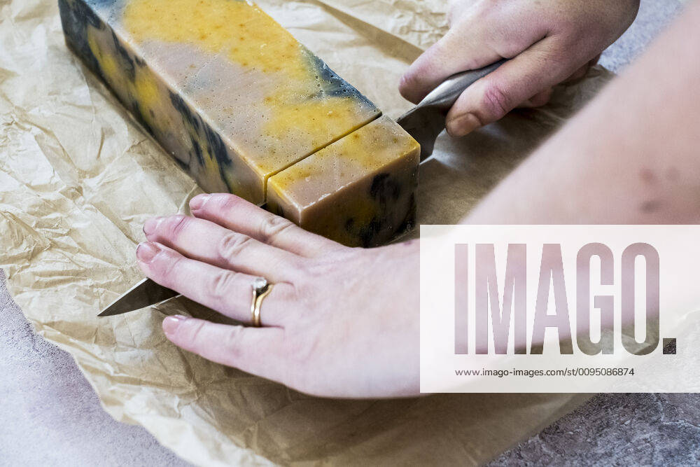 High angle close up person cutting yellow and black homemade bar of soap with kitchen knife. High angle close up person cutting yellow and black homemade bar of soap with kitchen knife. 59315