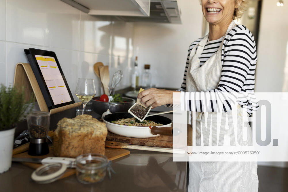 Happy mature woman with tablet cooking pasta dish in kitchen at home model released Symbolfoto property released VABF02448