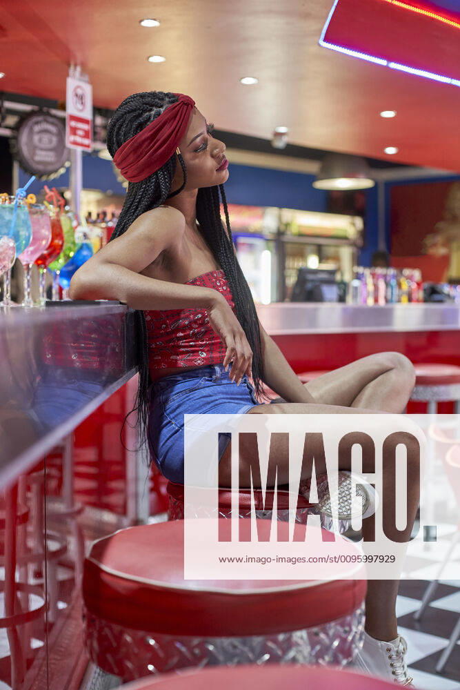 Young woman with braided hairstyle sitting on a bar on red stool model released Symbolfoto property released VEGF01159