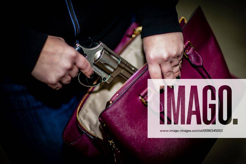 A womans hand takes a revolver out of a womans handbag held in front of her body, her finger is on the trigger Marbach , Baden Württemberg Germany