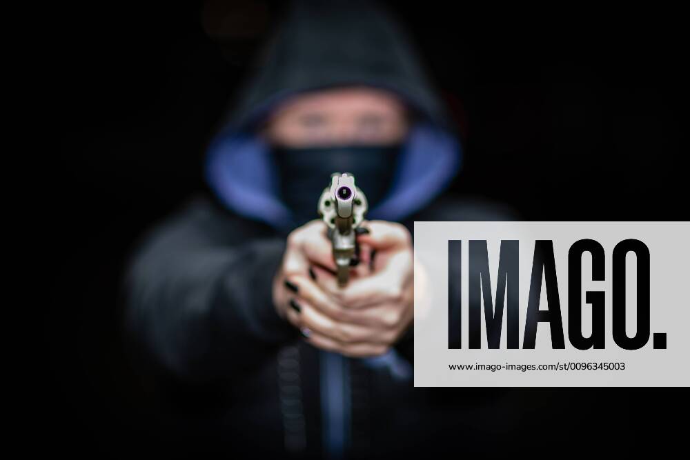 A woman in a hooded sweater, masked with her hands on a revolver looking into the barrel of a pistol Marbach , Baden Württemberg Germany