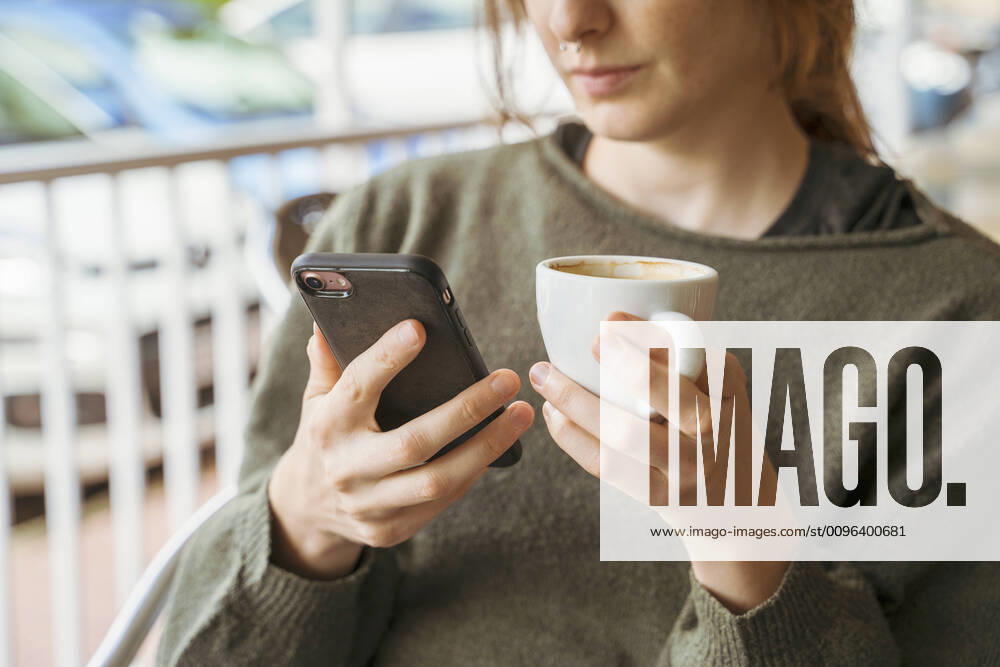 Close-up of young woman using cell phone and holding coffee cup model released Symbolfoto AFVF04839