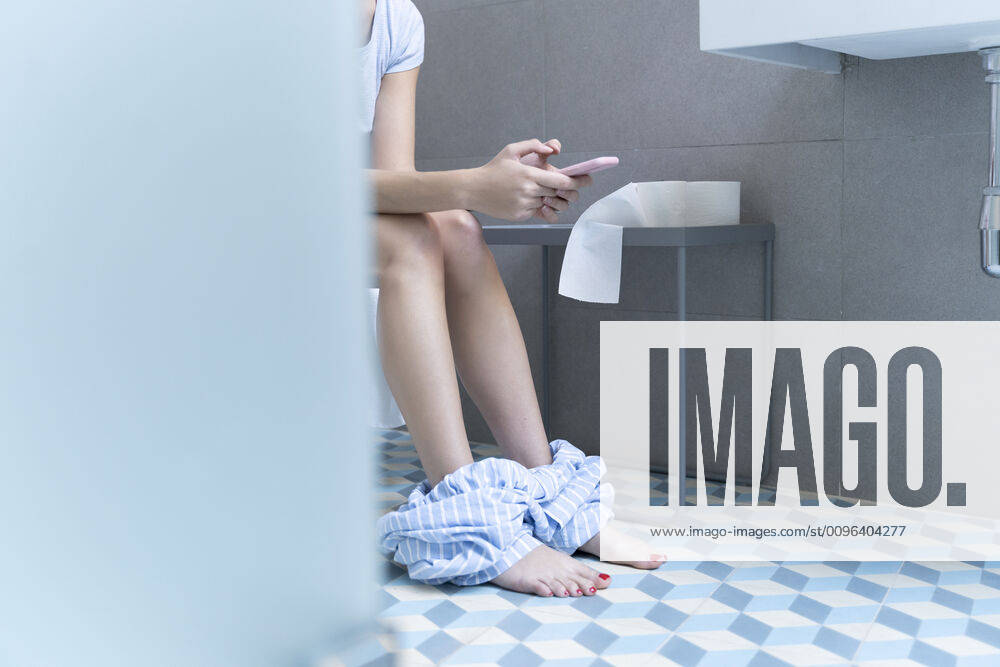 Young woman sitting on toilet and using smartphone model released Symbolfoto property released ERRF02554