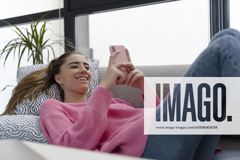 Portrait of happy young woman lying on the couch using cell phone model released Symbolfoto property released ERRF02579