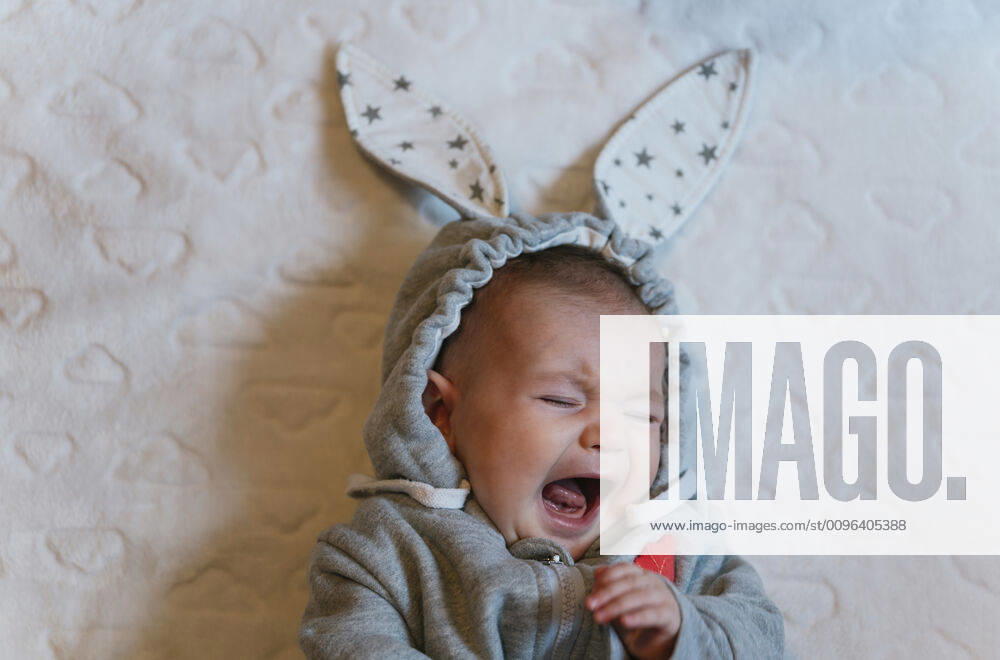 Portrait of crying baby girl in a rabbit hoodie lying on white blanket model released Symbolfoto GEMF03380