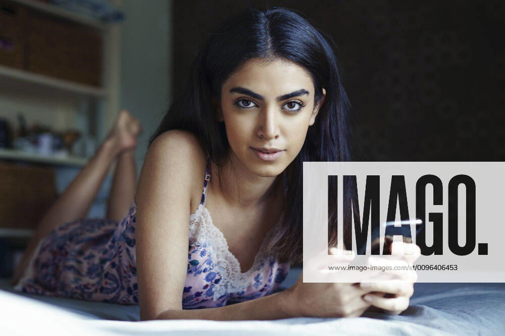 Portrait of young woman lying on bed with smartphone model released Symbolfoto JSMF01429