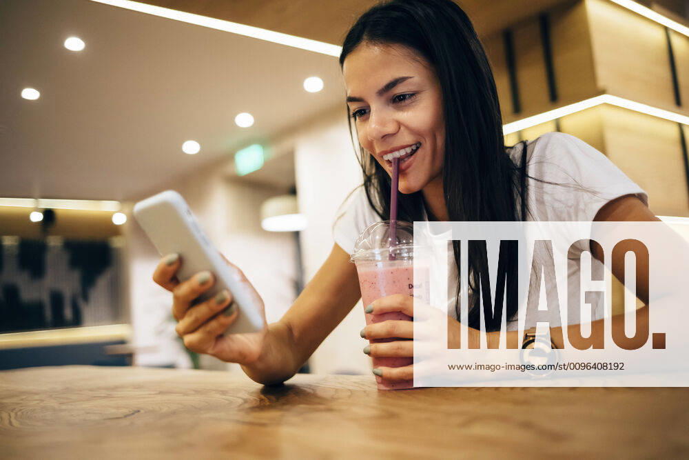 Black-haired woman drinking a smoothie and using smartphone in cafe model released Symbolfoto OYF00102