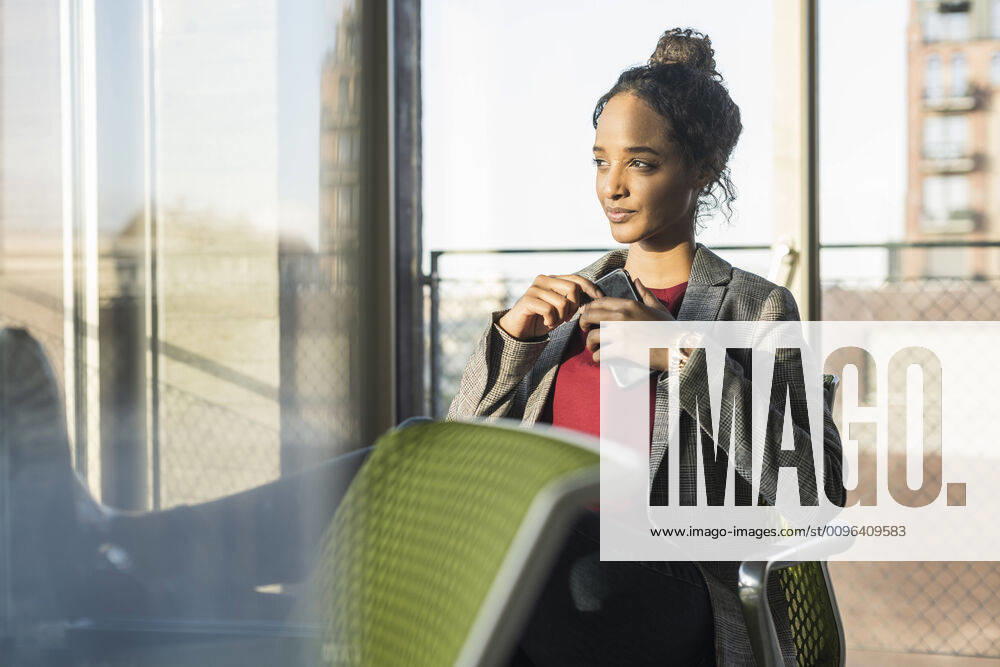 Young businesswoman with cell phone sitting at the window in office model released Symbolfoto property released UUF20029