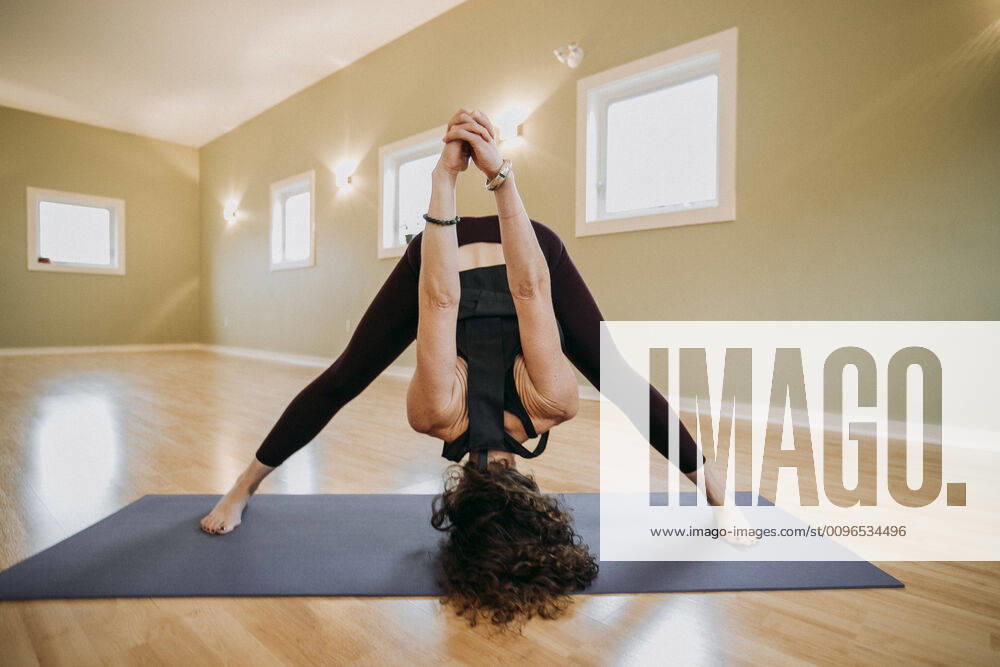 A woman stretches her hamstring on a yoga mat in a yoga studio Scarborough, ME, United States CR_SSNF191216B-253464-01