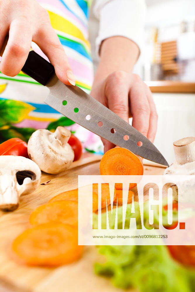 Woman s hands cutting vegetables Woman s hands cutting carrot, behind fresh vegetables.