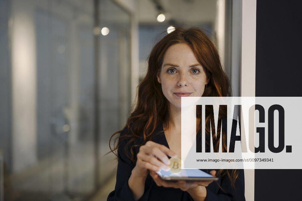 IMAGO Creative: 2022 Aussichten IMAGO Creative: 2021 Trends Portrait of redheaded woman holding bitcoin and tablet on office floor model released Symbolfoto property released KNSF07182