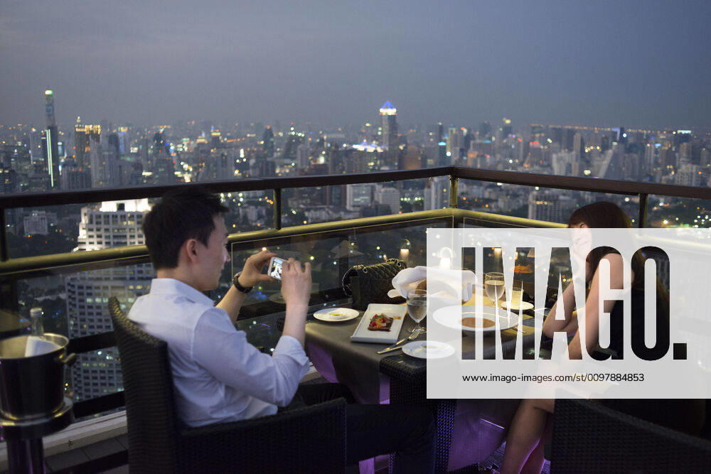 Romantic dinner. Banyan Tree Rooftop Vertigo & Moon Bar, Restaurant, , Bangkok , Thailand. View of the city, Vertigo Bar and Restaurant, roof of the Banyan Tree Hotel, at dusk Bangkok, Thailand, Asia. Reaching for the clouds at Vertigo and Moon Bar on the 61st floor of the Banyan Tree hotel is one of the best ways to end a long day in Bangkok. There is no lack of rooftop bars in town but Vertigo has always been amongst the favourites. With an unusual narrow and elongated shape, the entire top of the building is occupied by both the bar and the restaurant and gives the unusual impression of being aboard a spaceship in the sky. Located on Sathorn road, a very large busy avenue peppered with tall glass and metal skyscrapers and not far from the Lumpini park and Silom area, Banyan Tree is a name often associated with luxury. The hotel and its