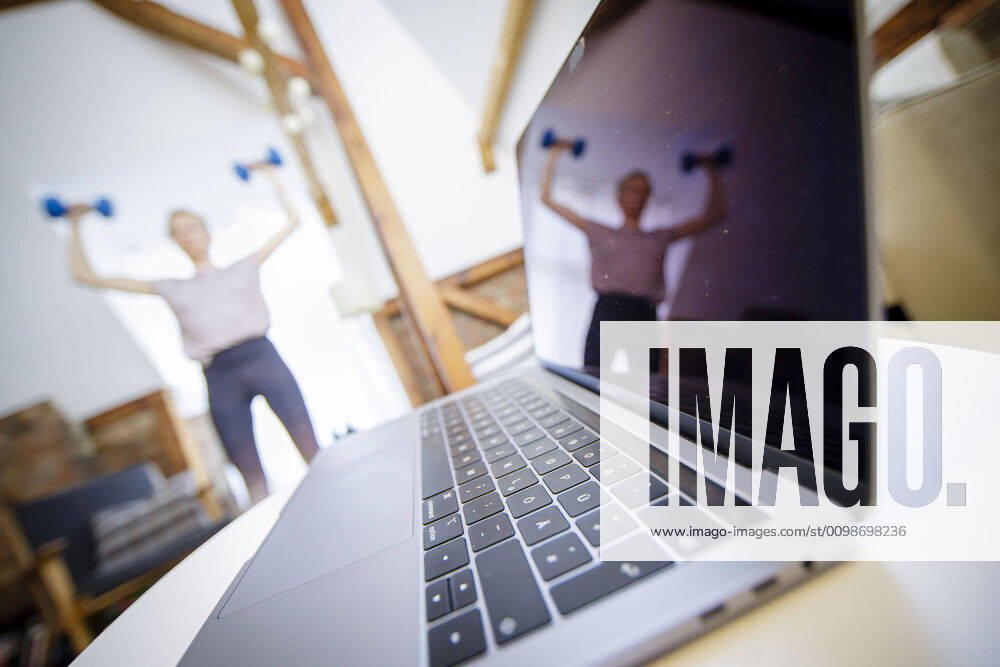 Symbolic photo on the subject of fitness A woman is exercising at home with dumbbells Next to her is a laptop Berlin, 26 03 2020 Berlin Germany