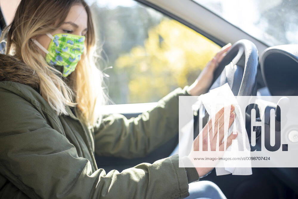 Young woman disinfects steering wheel in car