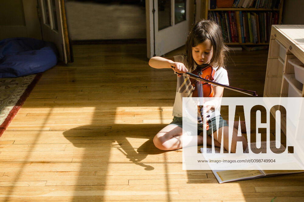 IMAGO Creative: Bildung, Musikerziehung A small girl sits on floor playing violin in front of open music book Columbus, OH, United States ,model released, Symbolfoto CR_RETI200313-313226-01