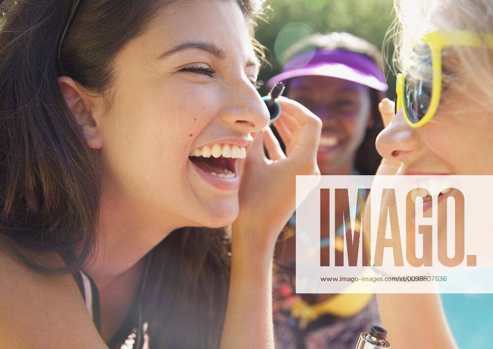 Happy teenage girl friends applying mascara on sunny patio England Kent