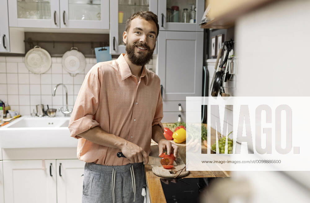 Young man standing in kitchen, chopping tomatoes, smiling model released Symbolfoto property released PESF01808
