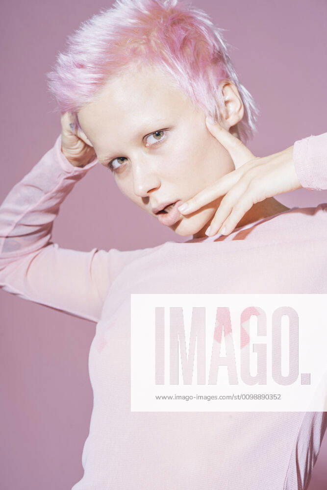 IMAGO Creative, Lifestyle, Barbiecore Portrait of young woman with short pink hair wearing pink top in front of pink background model released Symbolfoto VPIF02107