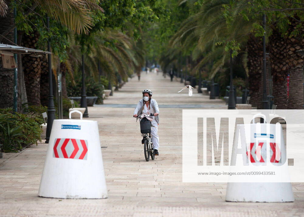 A woman wearing a face mask rides her bike along an a empty promenade during the covid-19 crisis..Following the confinement decreed by the Spanish government and will extended until 10th May, people are confinement in their homes causing an exceptional situation of unusual urban scenes such as empty streets. Malaga Spain - ZUMAs197 20200416_zaa_s197_047