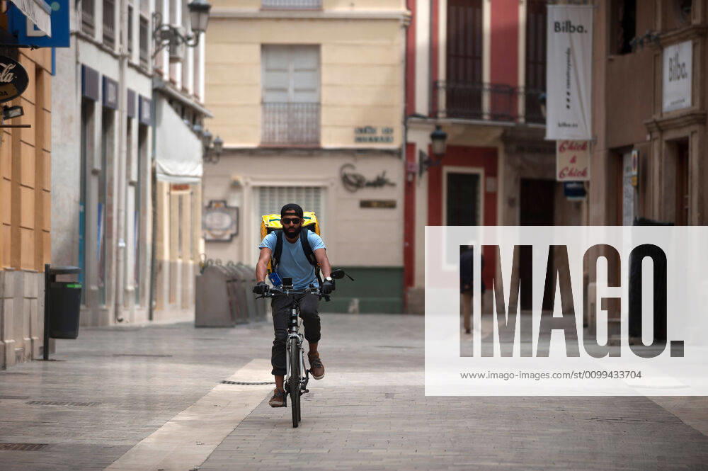 A Glovo delivery man rides his bike along an empty street during the covid-19 crisis..Following the confinement decreed by the Spanish government and will extended until 10th May, people are confinement in their homes causing an exceptional situation of unusual urban scenes such as empty streets. Malaga Spain - ZUMAs197 20200416_zaa_s197_056