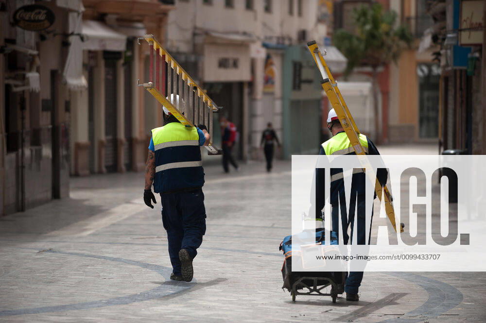 Construction workers walking on an almost deserted street during the covid-19 crisis..Following the confinement decreed by the Spanish government and will extended until 10th May, people are confinement in their homes causing an exceptional situation of unusual urban scenes such as empty streets. Malaga Spain - ZUMAs197 20200416_zaa_s197_058