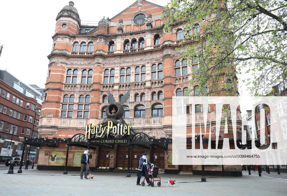 Day Twenty Six of Lockdown in London. A couple, in face masks and gloves, walk their dogs past the Palace Theatre which should have been showing Harry Potter and The Cursed Child. The country is on lockdown due to the COVID-19 Coronavirus pandemic. People are not allowed to leave home except for minimal food shopping, medical treatment, exercise - once a day, and essential work. COVID-19 Coronavirus lockdown, London, UK, on April 18, 2020