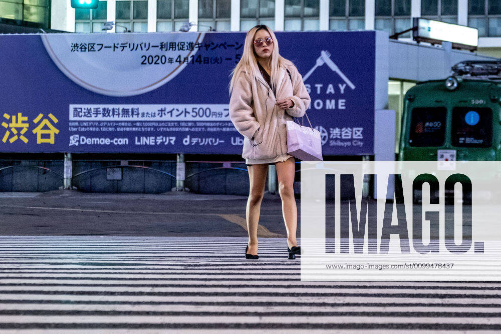 A woman crosses the street with lights off and restaurants closed in Shibuya area during the covid-19 crisis..The Japan government declared a state of emergency to cover the whole country and will continue until May 6. Tokyo governor, Yuriko Koike has asked restaurants and bars to be closed at 8pm as a preventive measure against COVID-2019. Tokyo Japan - ZUMAs197 20200419_zaa_s197_072