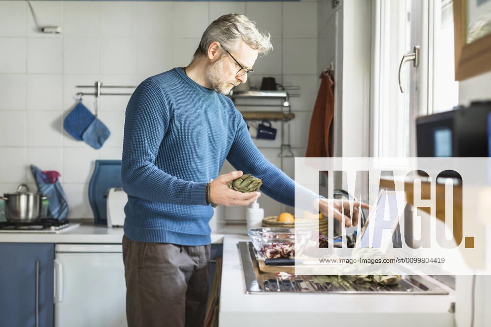 Mature man preparing salad in his kitchen using digital tablet model released Symbolfoto property released MCVF00259