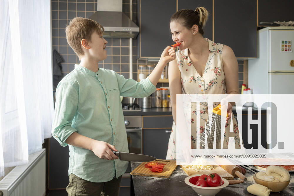 Boy feeding his mother with tomato slice in the kitchen model released Symbolfoto property released VPIF02215
