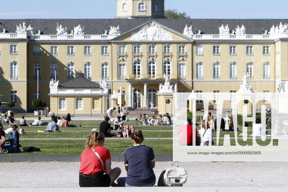 People sit on the lawns on the Schlossplatz in front of the Landesmuseum and the palace, respecting the rules of distance, and enjoy the warm spring day in the city centre of Karlsruhe, r City centre of Karlsruhe, Baden Württemberg, Germany