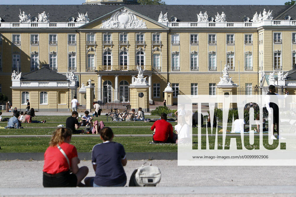 People sit on the lawns on the Schlossplatz in front of the Landesmuseum and the palace, respecting the rules of distance, and enjoy the warm spring day in the city centre of Karlsruhe, r City centre of Karlsruhe, Baden Württemberg, Germany