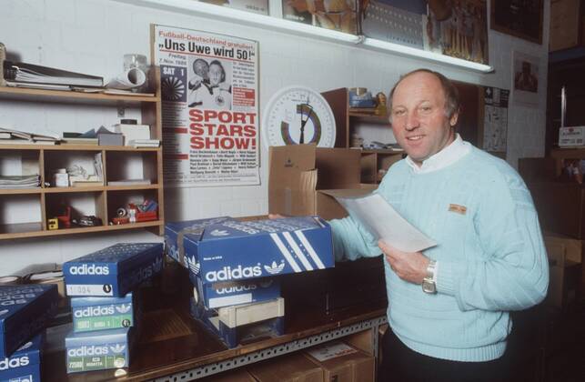 Uwe Seeler (Ex-Fußballnationalspieler) 10 86 ru Mann Fußball Nationalmannschaft grauhaarig Halbglatze leger Pullover Hemd stehend Keller Poster Fotografie Karton Schuh Unterlagen Papier haltend halb quer