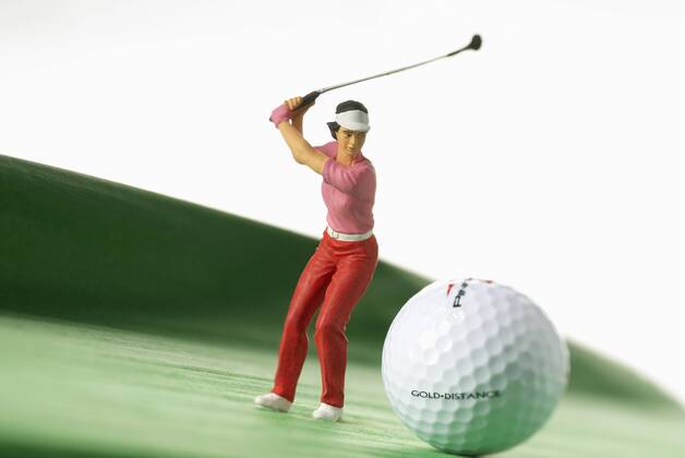 Symbolbild Golfspielen, eine Golferin als Figur schlägt den Ball auf dem Platz Ballposition