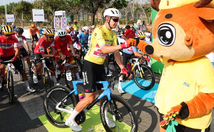 (250409) -- BAOTING, April 9, 2025 -- Norman Vahtra of China Glory-MENTECH Continental Cycling Team reacts with the mascot before Stage 3 at the 16th Tour of Hainan cycling race from Lingshui to Baoting, south China s Hainan Province, April 9, 2025. ) (SP)CHINA-HAINAN-BAOTING-CYCLING-TOUR OF HAINAN (CN) YangxGuanyu 