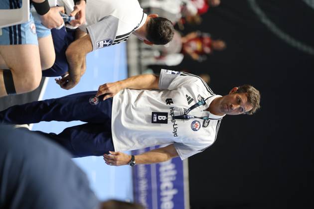 Torsten Jansen, head coach of HSV Hamburg, stands focused on the sidelines at the Volkswagen Halle in Braunschweig. In the foreground, an HSV Hamburg player sits on the bench. Torsten Jansen of HSV Hamburg watches the game from the sidelines. Copyright: xspeedshotx