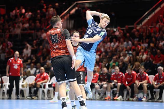Moritz Sauter, No. 33 of HSV Hamburg, jumps and takes a shot while a player from MTV Braunschweig 86 tries to block the shot. The packed Volkswagen Halle in Braunschweig serves as the backdrop as Moritz Sauter, No. 33 of HSV Hamburg, takes a jump shot against MTV Braunschweig. Copyright: xspeedshotx