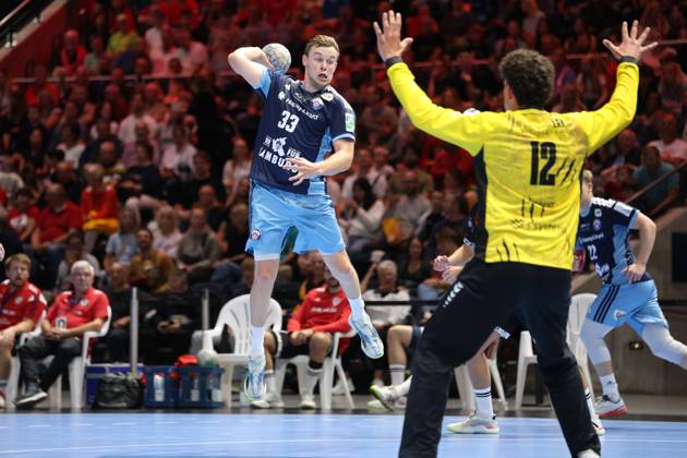 Moritz Sauter, No. 33 of HSV Hamburg, jumps and goes up for a shot, while goalkeeper Timon Serbest, No. 12 of MTV Braunschweig, spreads his arms. Another HSV player can be seen in the background. Moritz Sauter, No. 33 of HSV Hamburg, takes a jump shot against MTV Braunschweig. Copyright: xspeedshotx