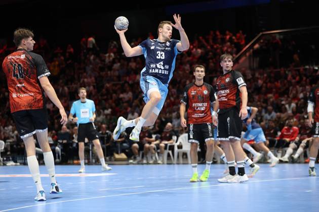 Moritz Sauter, 33, of HSV Hamburg, jumps for a shot at the Volkswagen Halle in Braunschweig; the ball is in his raised shooting hand. Several MTV Braunschweig players watch the play from the background, including Tim Lietz. Moritz Sauter, 33, of HSV Hamburg, takes a jump shot against MTV Braunschweig. Copyright: xspeedshotx