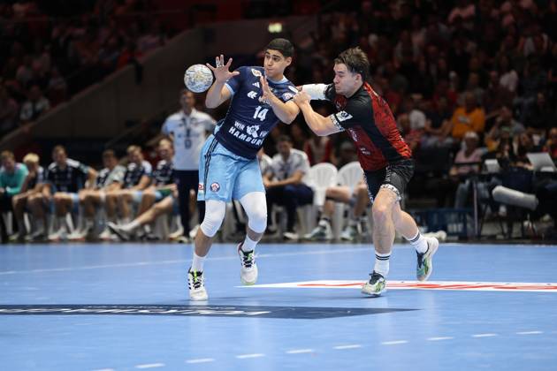 Mahmoud El Shobaky, No. 14, of HSV Hamburg, is pulling away for a shot while being pressured by a player from MTV Braunschweig. The ball is already in flight, the scene shows intense physical play at the Volkswagen Halle in Braunschweig. Mahmoud El Shobaky (14) of HSV Hamburg is locked in a battle for the ball as he attempts a shot Copyright: xspeedshotx