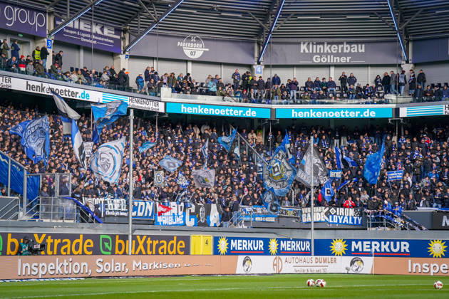 Germany Soccer Bundesliga 2026–2027, Matchday 7: SC Paderborn vs. Hamburger SV at Home Deluxe Arena in Paderborn. Home and away fans of Hamburger SV (HSV) in the visitors’ section of the Home Deluxe Arena in Paderborn. A densely packed visitors’ section with numerous blue, white, and black flags, fan banners, banners, and scarves. Fan culture, ultras, organized fan scene, away game, soccer, Bundesliga, spectators, atmosphere, support, fan section, stands, wide shot, stadium, sports venue, security fence, advertising, sponsors, advertising banners, Merkur, buXtrade, HENKENOTTER Copyright: xJOERANxSTEINSIEKx