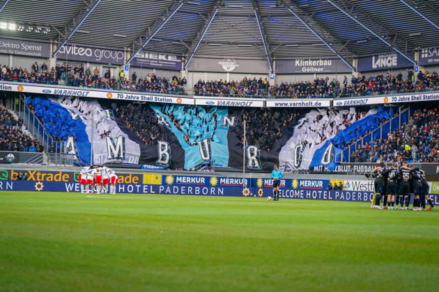 Germany Soccer Bundesliga 2026–2027, Matchday 7: SC Paderborn vs. Hamburger SV at Home Deluxe Arena, Paderborn. Interior view of the Home Deluxe Arena in Paderborn featuring a large blue, black, and white choreographed display by the home fans of SC Paderborn 07, with HAMBURG lettering. Fans, Ultras, fan choreography, fan scene, flags, spectators, stands, fan section, atmosphere, pre-match team circles for SC Paderborn and Hamburger SV, soccer, Bundesliga, stadium, sports venue, wide shot, playing field, referee, floodlights, advertising, sponsors, advertising banners, Merkur, buXtrade, Varnholt, Welcome Hotel Copyright: xJOERANxSTEINSIEKx
