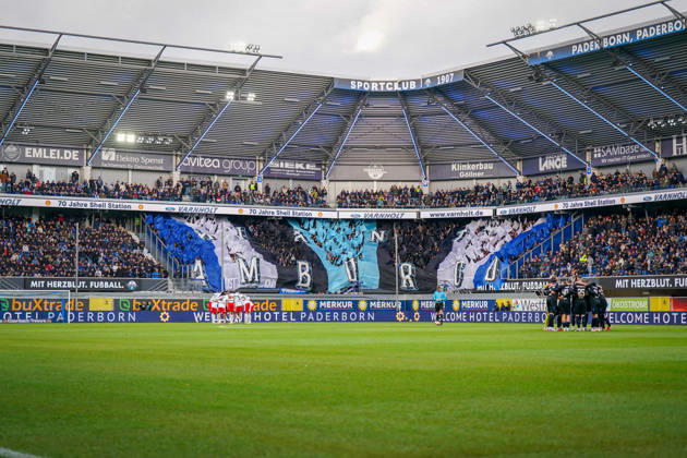 Germany Soccer Bundesliga 2026–2027, Matchday 7: SC Paderborn vs. Hamburger SV at Home Deluxe Arena, Paderborn. Interior view of the Home Deluxe Arena in Paderborn featuring a large blue, black, and white choreographed display by the home fans of SC Paderborn 07, with HAMBURG lettering. Fans, Ultras, fan choreography, fan scene, flags, spectators, stands, fan section, atmosphere, pre-match team circles for SC Paderborn and Hamburger SV, soccer, Bundesliga, stadium, sports venue, wide shot, playing field, referee, floodlights, advertising, sponsors, advertising banners, Merkur, buXtrade, Varnholt, Welcome Hotel Copyright: xJOERANxSTEINSIEKx