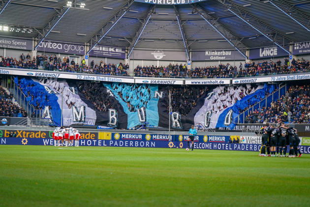 Germany Soccer Bundesliga 2026–2027, Matchday 7: SC Paderborn vs. Hamburger SV at Home Deluxe Arena, Paderborn. Interior view of the Home Deluxe Arena in Paderborn featuring a large blue, black, and white choreographed display by the home fans of SC Paderborn 07, with HAMBURG lettering. Fans, ultras, fan choreography, fan scene, flags, spectators, stands, fan section, atmosphere, pre-match team circles for SC Paderborn and Hamburger SV, soccer, Bundesliga, stadium, sports venue, wide shot, playing field, referee, floodlights, advertising, sponsors, advertising banners, Merkur, buXtrade, Varnholt, Welcome Hotel Copyright: xJOERANxSTEINSIEKx