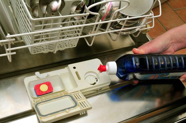 Hand füllt Glasreiniger in eine Spülmaschine