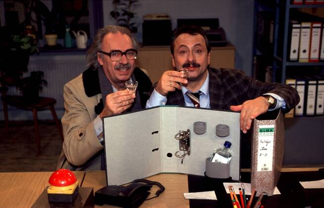 Wolfgang Stumph (re.) mit Achim Wolff in Salto Kommunale (ZDF) 01 98 te Fernsehen TV Schauspiel Komik Serie Film Szene Kulisse Studio Dekoration Tisch Schreibtisch Büro sitzend Flasche Getränk ALKOHOL Schnaps Glas haltend Ordner halb quer Gespräch