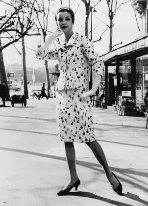 Paris Spring ensemble by Givenchy for this coming season. Medium is blue flowered printed white shantung. The material is softly gathered in the back. The long sleeved wide collared jacket stops at the hip line and is held tight by four white shantung covered buttons in front. A navy blue straw hat and white kid gloves complete the ensemble 1965 UnitedArchives00507316 