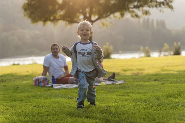 Happy boy running on meadow with family in background model released Symbolfoto  PAF001200