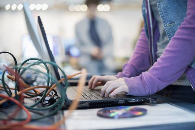 A person using a laptop computer. Disc and wires on the counter. Repair shop.  15213