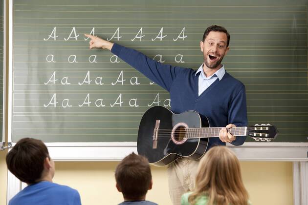 IMAGO Creative: Bildung, Musikerziehung Teacher with guitar at blackboard showing variations of letter A model released Symbolfoto property released  MFRF000110